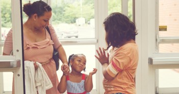 Stock photo of three Latina women of different ages - one middle age, one child, and one teenager - greeting each other at a door