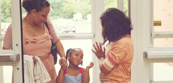 Stock photo of three Latina women of different ages - one middle age, one child, and one teenager - greeting each other at a door