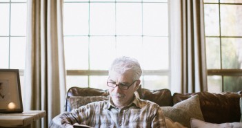 Stock photo of an older white man sitting on a sofa and reading in his living room