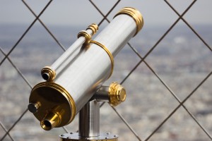 Stock photo of a silver and gold telescope looking over a city from behind a chain-fence