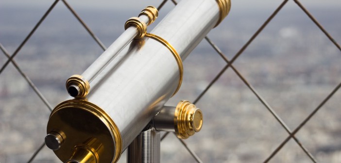 Stock photo of a silver and gold telescope looking over a city from behind a chain-fence