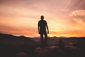 Stock photo of a silhouette of a man on top of a mountain looking at either a sunrise or a sunset