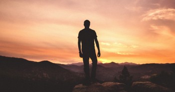 Stock photo of a silhouette of a man on top of a mountain looking at either a sunrise or a sunset