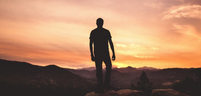 Stock photo of a silhouette of a man on top of a mountain looking at either a sunrise or a sunset