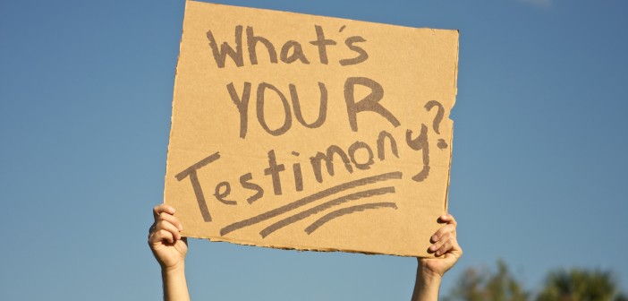 Stock art of someone holding up a cardboard sign that says "WHAT'S YOUR TESTIMONY?"