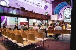 Stock photo of a mostly empty worshiping space with some people listening to a sermon
