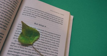 Stock photo of a book opened up to a page with a green leaf marking where the reader left off