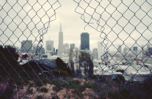 Stock photo of a fence with a hole in it overlooking a city skyline