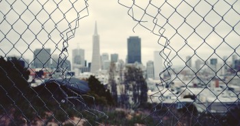 Stock photo of a fence with a hole in it overlooking a city skyline