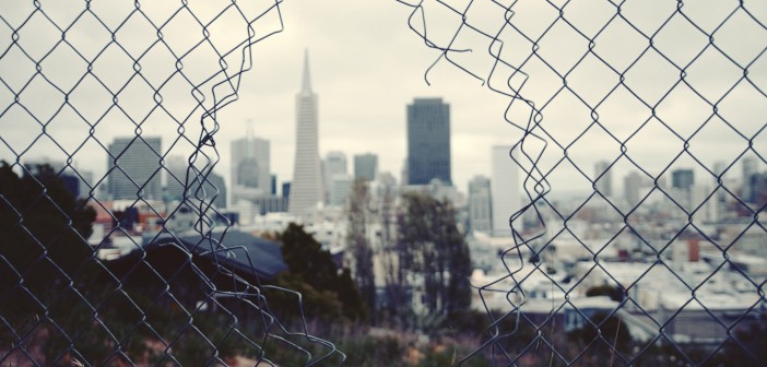 Stock photo of a fence with a hole in it overlooking a city skyline
