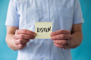Stock photo of a white person holding a post-it note that says "LISTEN"