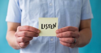 Stock photo of a white person holding a post-it note that says "LISTEN"