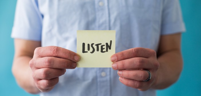 Stock photo of a white person holding a post-it note that says "LISTEN"