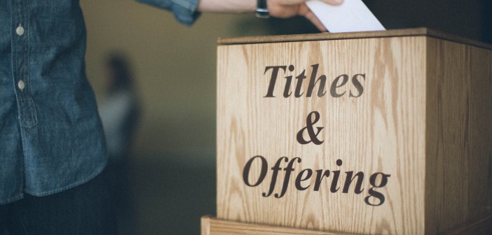 Stock photo of someone putting an envelope in a box labeled "Tithes & Offering"