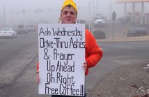 Person standing outside on the side of the road holding a sign that reads “Ash Wednesday Drive-Thru Ashes & Prayer Up Ahead on Right. Free Coffee!!”