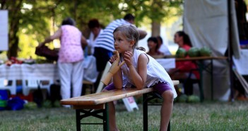 Stock photo of a young white girl sitting on a bench at a community picnic