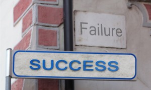 Stock photo of a street sign that says "SUCCESS" on it with a sign that says "FAILURE" in the background