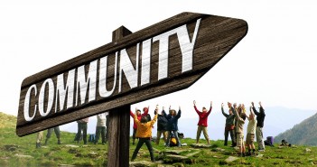 Stock photo of a signpost that points to "COMMUNITY" with a group of people standing in a circle behind it