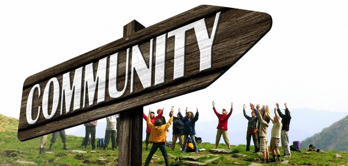Stock photo of a signpost that points to "COMMUNITY" with a group of people standing in a circle behind it