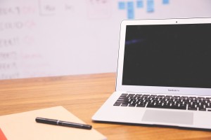Stock photo of a MacBook Air that is opened, but turned off on a desk with a blank piece of paper and a black pen