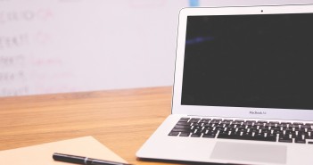 Stock photo of a MacBook Air that is opened, but turned off on a desk with a blank piece of paper and a black pen