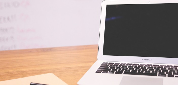 Stock photo of a MacBook Air that is opened, but turned off on a desk with a blank piece of paper and a black pen