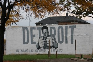 Stock photo of a white wall with "DETROIT restaurant and food service" and a young African American man with his fists up painted on it