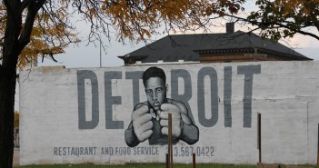 Stock photo of a white wall with "DETROIT restaurant and food service" and a young African American man with his fists up painted on it