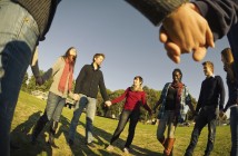 The New Realities of Engaging Newcomers Photo of a diverse group of young adults holding hands in a circle under a blue sky