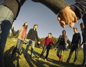 Photo of a diverse group of young adults holding hands in a circle under a blue sky
