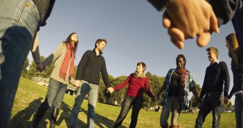 Photo of a diverse group of young adults holding hands in a circle under a blue sky