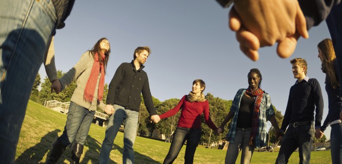 Photo of a diverse group of young adults holding hands in a circle under a blue sky