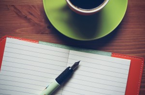 Photo of pen and paper on a table top with cup of coffee
