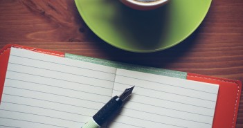 Photo of pen and paper on a table top with cup of coffee