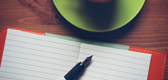 Photo of pen and paper on a table top with cup of coffee