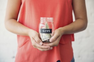 Photo of a young person holding a glass jar of money marked "Give"