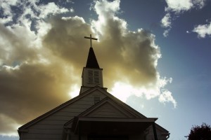 Photo of a church steeple backlit by the sun and clouds