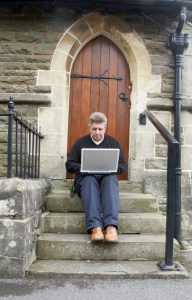 Photo of a person sitting on the front church steps working on a laptop computer