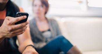 Stock photo of a young African American male on his smart phone and a young white woman looking annoyed at him