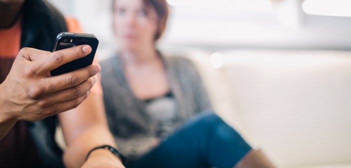 Stock photo of a young African American male on his smart phone and a young white woman looking annoyed at him