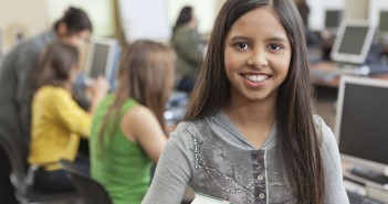 Photo of a smiling girl holding schoolbooks in a classroom