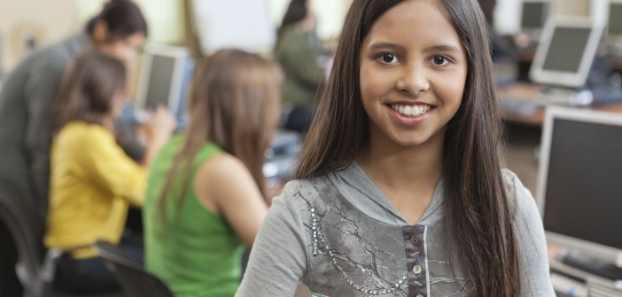 Photo of a smiling girl holding schoolbooks in a classroom