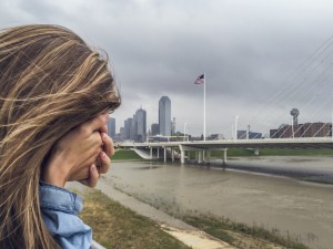 Stock photo of a woman with her face buried in her hand standing by a city waterfront