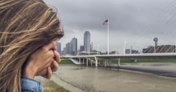Stock photo of a woman with her face buried in her hand standing by a city waterfront