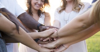 Stock photo of a group of smiling people with their hands all-in in a manner similar to how a sports team would end a huddle