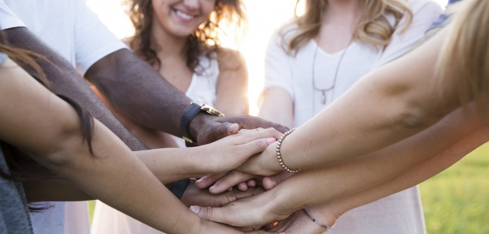 Stock photo of a group of smiling people with their hands all-in in a manner similar to how a sports team would end a huddle