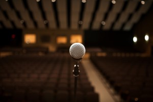 Stock photo of a stand microphone presumably on a stage facing an empty auditorium