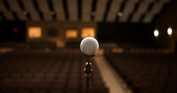 Stock photo of a stand microphone presumably on a stage facing an empty auditorium