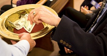 Image of a person placing money in an offering plate at church