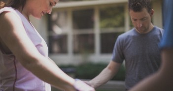 Stock photo of a group of at least three people holding hands in a circle and praying outside